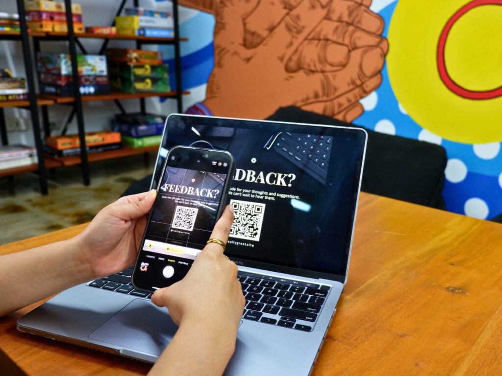 Hands with cell phone scanning a QR code in front of a laptop screen